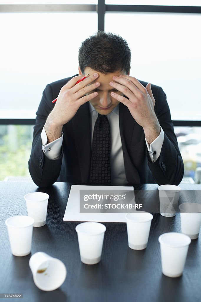 Reflective businessman sitting at table with plastic cups of coffee