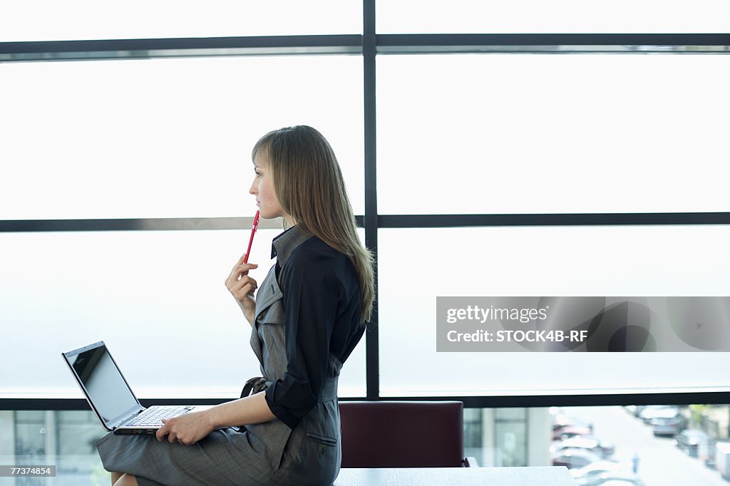 Reflective businesswoman cross-legged on table while using a laptop