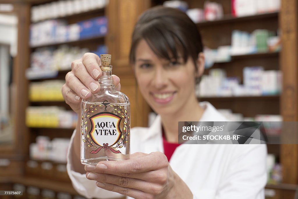 Female pharmacist holding a bottle of Aqua Vitae (aquavit, water of life) at camera