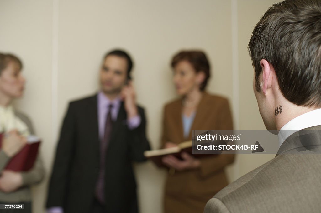 Businesspeople standing together, businessman with dollar sign tattoo in foreground