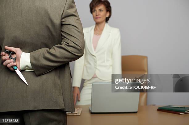 businessman holding scissors behind back, facing businesswoman in office - hiding behind laptop stock pictures, royalty-free photos & images