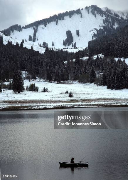 Fisherman crosses the Spitzingsee Lake in a boat in front of snow covered Alpine mountains on October 19, 2007 in Spitzingsee, Germany. Weather...