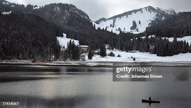 Fisherman crosses the Spitzingsee Lake in a boat in front of snow covered Alpine mountains on October 19, 2007 in Spitzingsee, Germany. Weather...