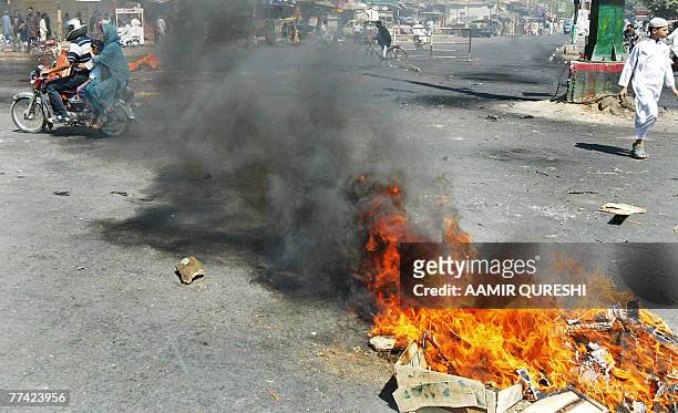 Pakistani man and his family drives a motorbike through burning tires, torched by angry supporters of former Pakistani prime minister Benazir Bhutto,...