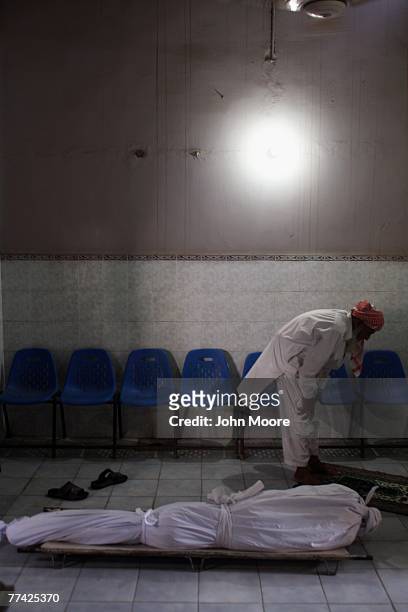 Worker prays next to an unclaimed body at the Edhi Foundation morgue October 20, 2007 in Karachi, Pakistan. Two days after a suicide bomber attacked...
