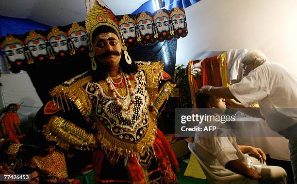 An Indian actor dressed as the evil king Ravana poses for the camera as his colleague has his make-up done during the Ramleela at the Maharashtra...