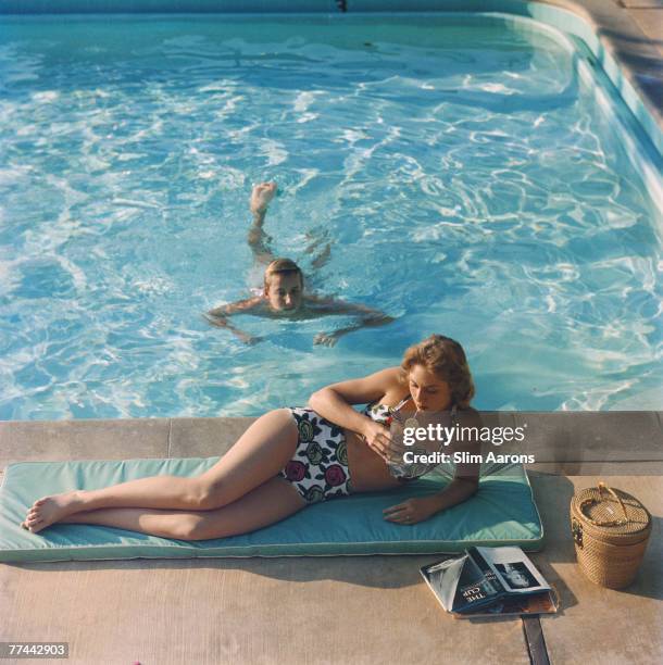 Diane Fletcher relaxing by a pool at the Kona Kai Club on Shelter Island, San Diego, California, 1960. She is wearing a two-piece swimsuit by Marie...