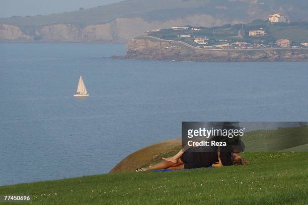 Young lovers kiss each other on a cliff overlooking a sailboat on the ocean August, 2007 in Gijon, Spain.