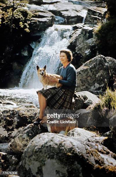 The Queen sitting on rocks beside a waterfall on the Garbh Allt burn with two corgis on the Estate at Balmoral Castle, Scotland during the Royal...