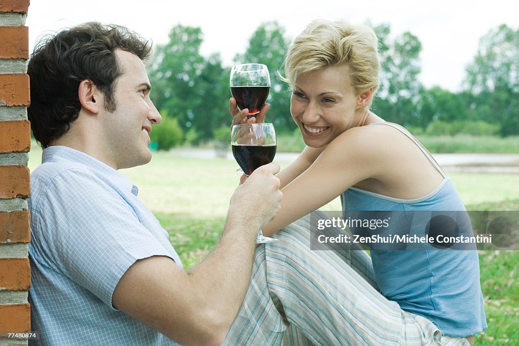 Couple sitting outdoors, toasting with glasses of red wine