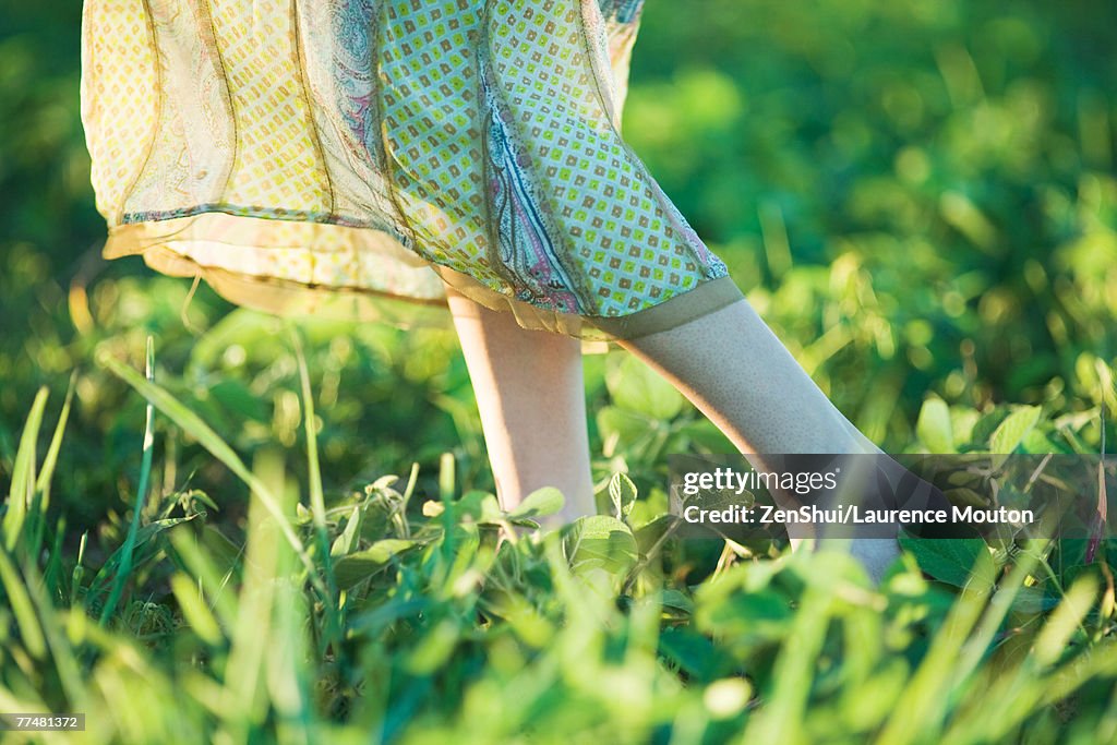 Young woman wearing long dress walking across grass, close-up, knee down