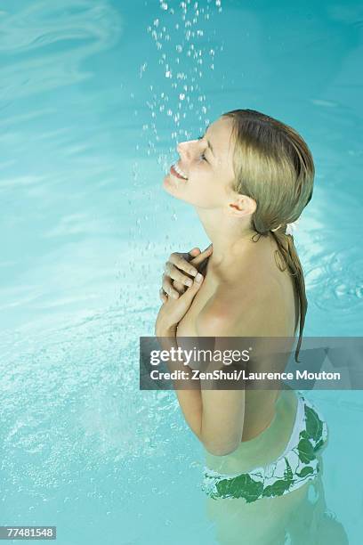 young woman standing under spray of water in pool, covering bare chest - bare bottom women stock-fotos und bilder