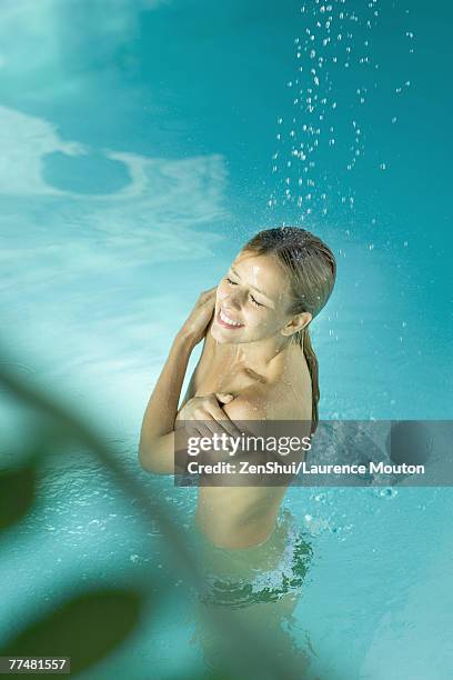 young woman standing under spray of water in pool, covering bare chest - bare bottom women stockfoto's en -beelden