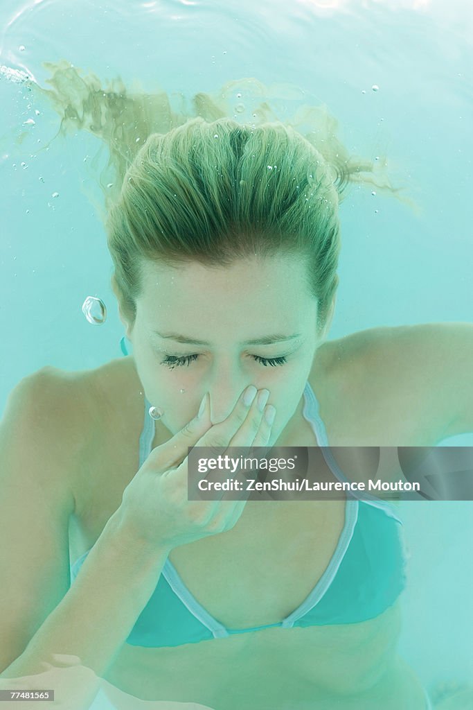 Young woman holding nose underwater