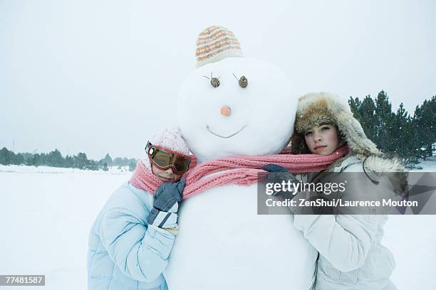 two friends hugging snowman - girl face hat raincoat stock pictures, royalty-free photos & images