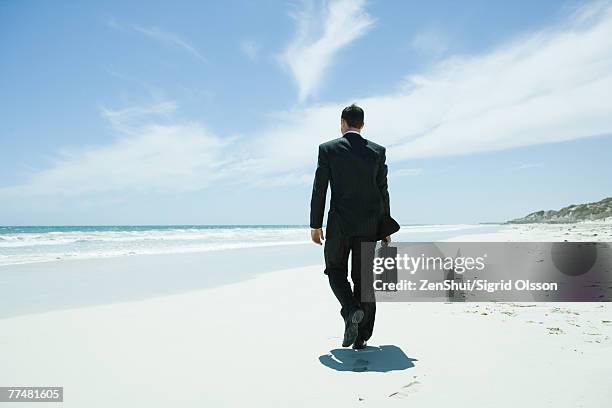 businessman walking on beach, carrying briefcase - mann anzug von hinten stock-fotos und bilder