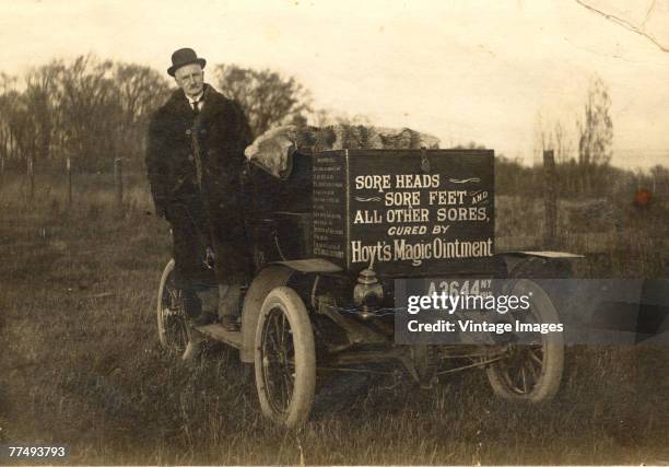 Pharmacological entrepreneur Leander Hoyt stands on the runner of his automobile, which is covered in advertisments for 'Hoyt's Magic Ointment' which...