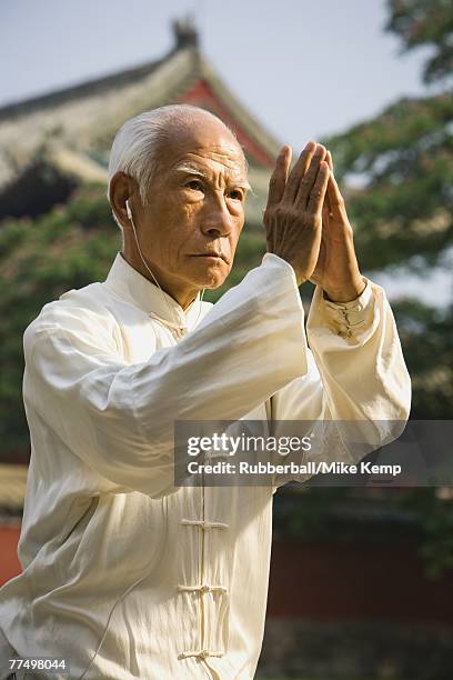 man standing outdoors doing kung fu with ear buds and pagoda in background - martial arts background stock pictures, royalty-free photos & images