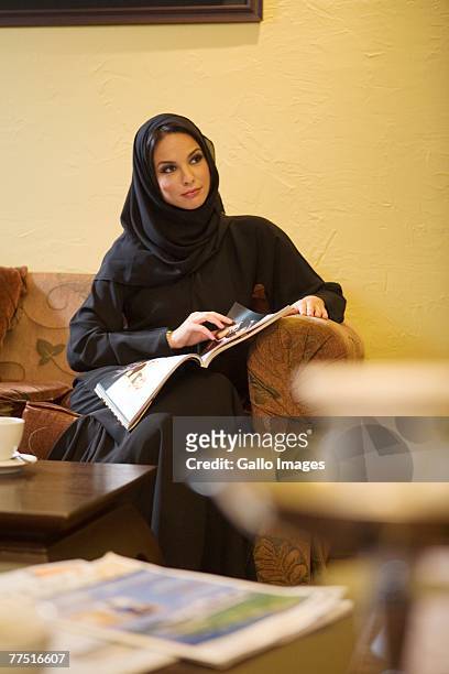 arab woman reading magazines on couch in living room. dubai, united arab emirates - pipe smoking women stock pictures, royalty-free photos & images