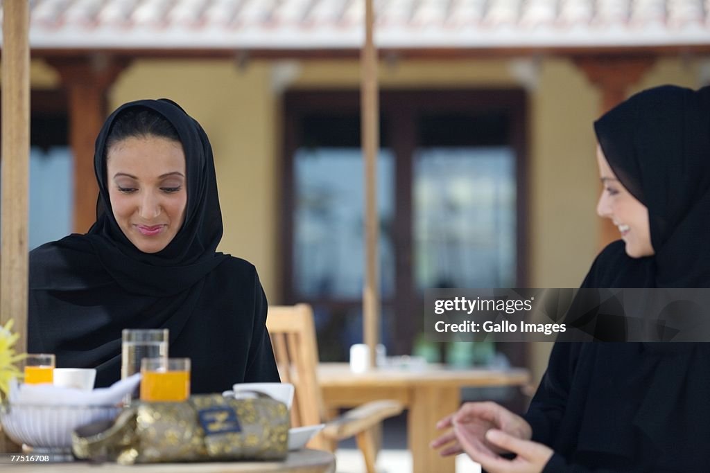 Two Arab women sitting on an outdoor patio, eating breakfast. Dubai, United Arab Emirates