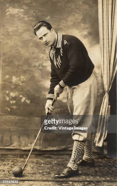 Studio portrait of an unidentified, well-dressed indoor golfer, who poses with a club and ball at the ready, Akron, Ohio, late 1800s or early 1900s.