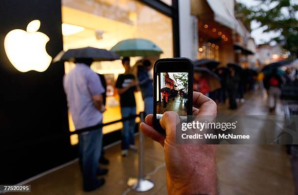 Customer takes pictures on his iPhone of other customers lined up outside an Apple store to purchase the new Apple computer operating system known as...