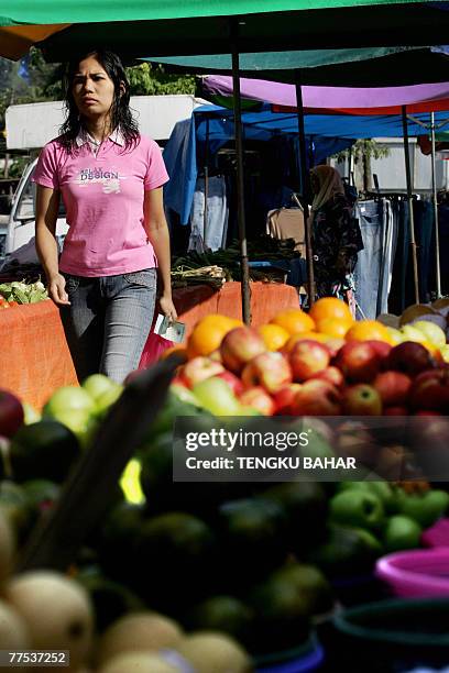 Customer, holding money in hand, walks past a row of fruit and vegetables for sale at an outdoor wet market in Kuala Lumpur, 28 October 2007....