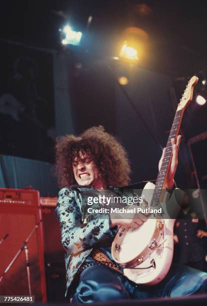 Singer Marc Bolan places a tambourine on the strings of his white Fender Stratocaster guitar as he performs with English glam rock group T-Rex at the...