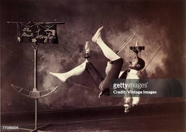 Publicity portrait of 'The Great Layton,' who reclines on a tightrope while he balances three oil lamps, early twentieth century.