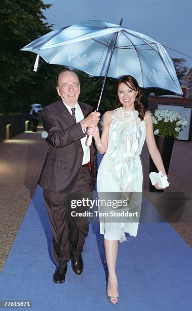 News Corporation Chairman and CEO Rupert Murdoch shelters his wife Wendi from the rain as they leave Mr Murdoch's annual Summer Party which was held...