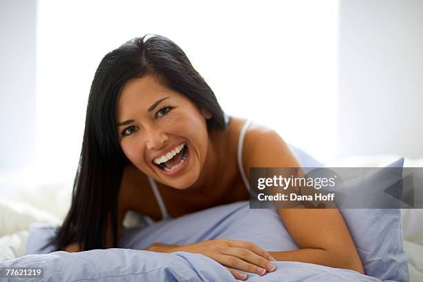 a young woman holds the cushion in her hands as she laughs in front of the camera - negligée stock-fotos und bilder