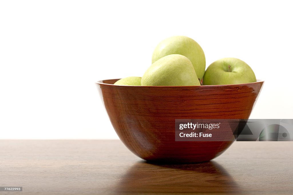 Green apples in polished brown wood bowl