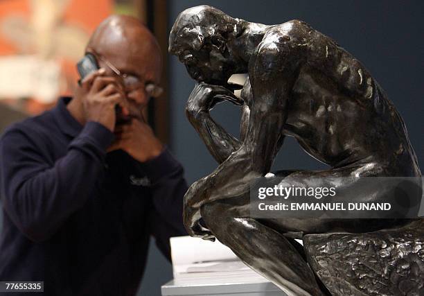 Sotheby's auction house employee talks on his mobile phone next to the sculpture "Le Penseur" by French artist Auguste Rodin during a preview of...