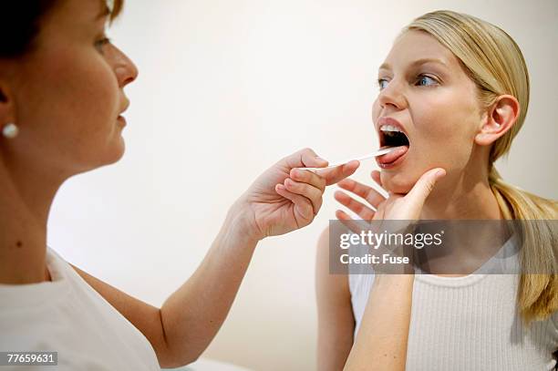 doctor examining female patient with tongue depressor - tongue depressor stock pictures, royalty-free photos & images