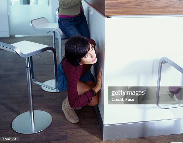 young woman hiding behind furniture peeping around the corner - 追う ストックフォトと画像