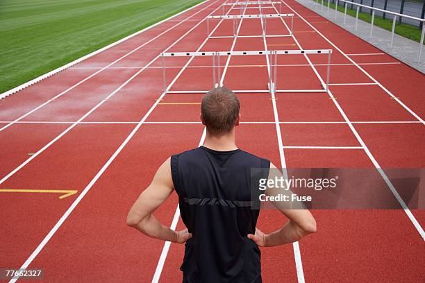 runner looking at hurdles - baanevenement mannen stockfoto's en -beelden