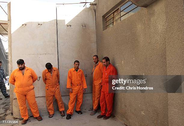 Arrested Iraqi men who've been chosen to appear before an Iraqi judge to be arraigned stand in orange jumpsuits to wait for the trip to the court...