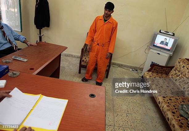 An arrested Iraqi man who's been chosen to appear before Iraqi judges stands in a makeshift courtroom listens while judges read charges against him...