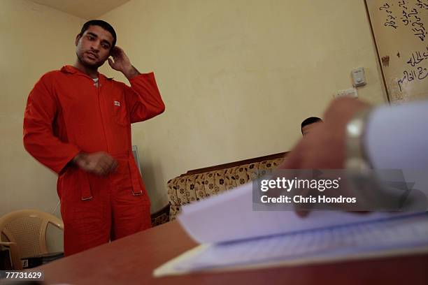 An arrested Iraqi man who's been chosen to appear before Iraqi judges stands in a makeshift courtroom listens while judges read charges against him...