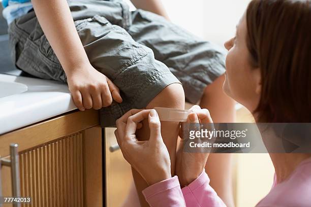 mother applying bandage to sons knee - wounded photos et images de collection