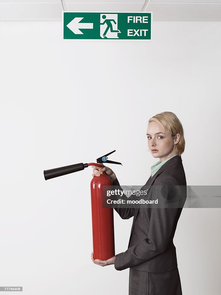 Businesswoman Holding Fire Extinguisher Under Exit Sign