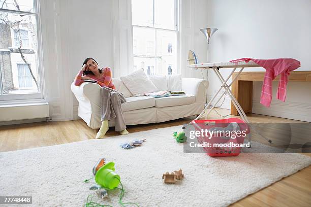 pensive housewife in messy living room - bügelbrett stock-fotos und bilder
