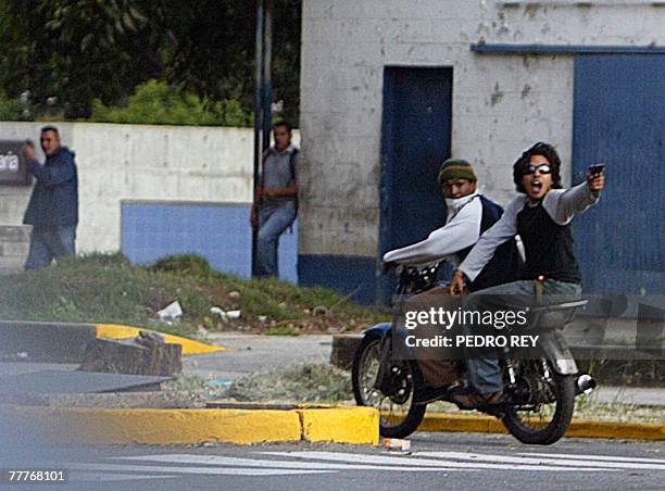 Young man riding piggyback on a motorcycle aims his handgun during clashes between opposition university students and pro-Chavez students before of a...