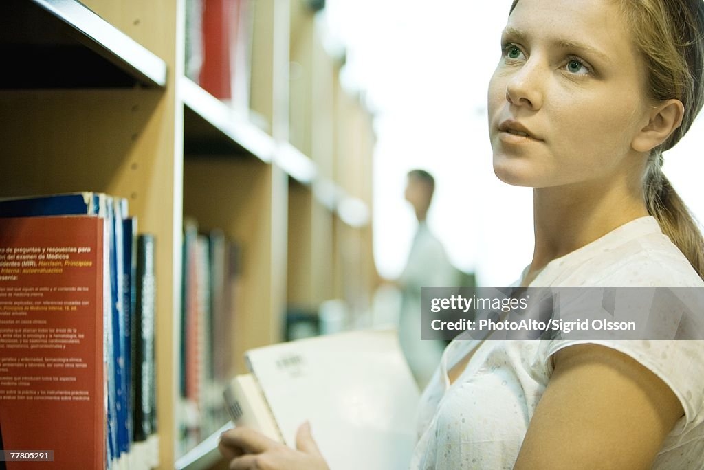 Young woman looking at shelves of books in library