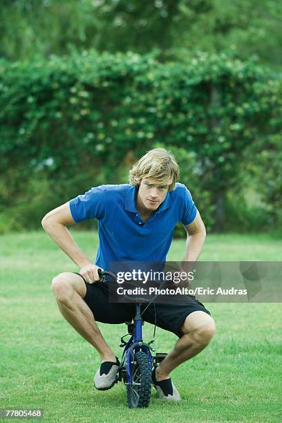 young man riding small bicycle, full length - too small stockfoto's en -beelden