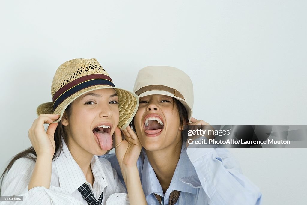 Two young friends wearing hats, sticking out tongues, looking at camera, portrait