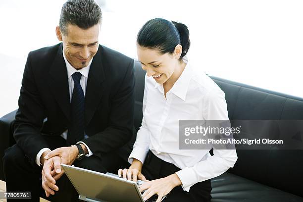 male and female business associates sitting in lobby, using laptop, smiling - white blouse stock-fotos und bilder