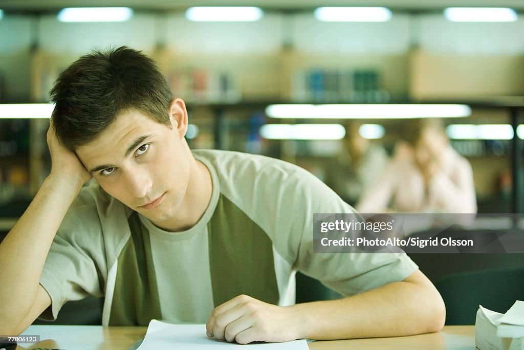 Male student studying in library, looking at camera