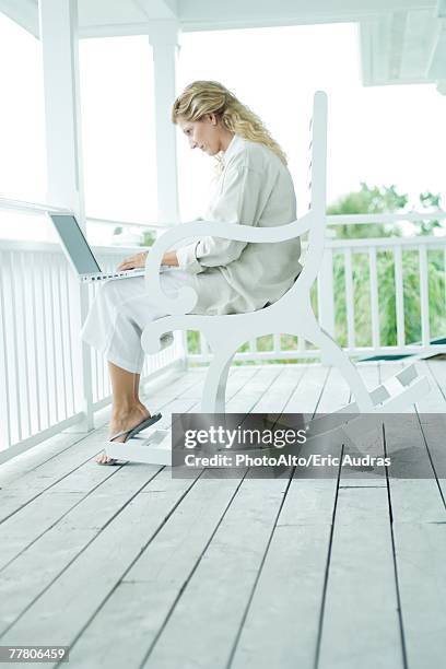 woman sitting in rocking chair on porch, using laptop computer, full length - auf dem schoß stock-fotos und bilder