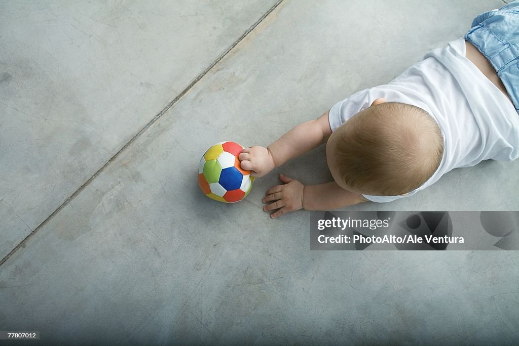 Baby crawling on floor, holding ball, view from directly above